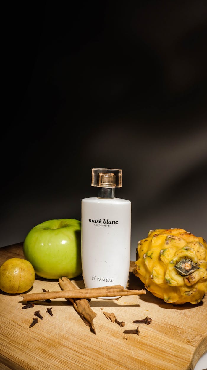 Still life of a perfume bottle with tropical fruits and spices on a wooden surface.